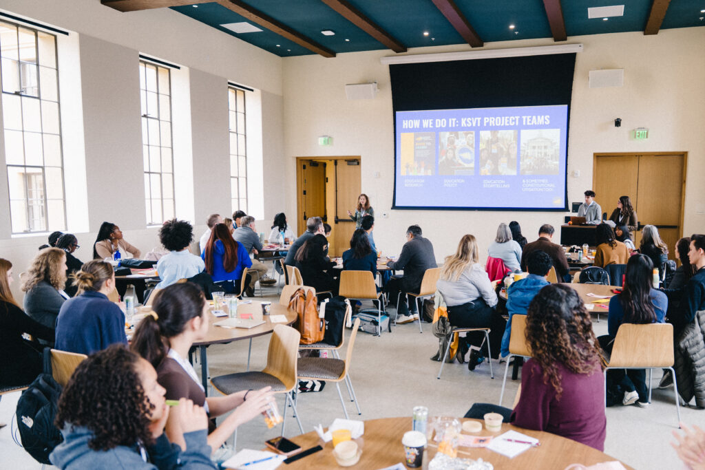A presenter talks in front of the room.