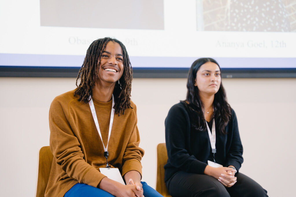 Two students smile while sitting on a panel.