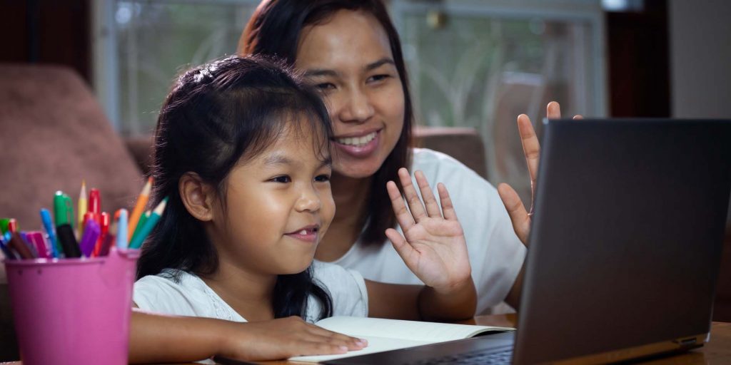 A mother and daughter wave to someone on a laptop