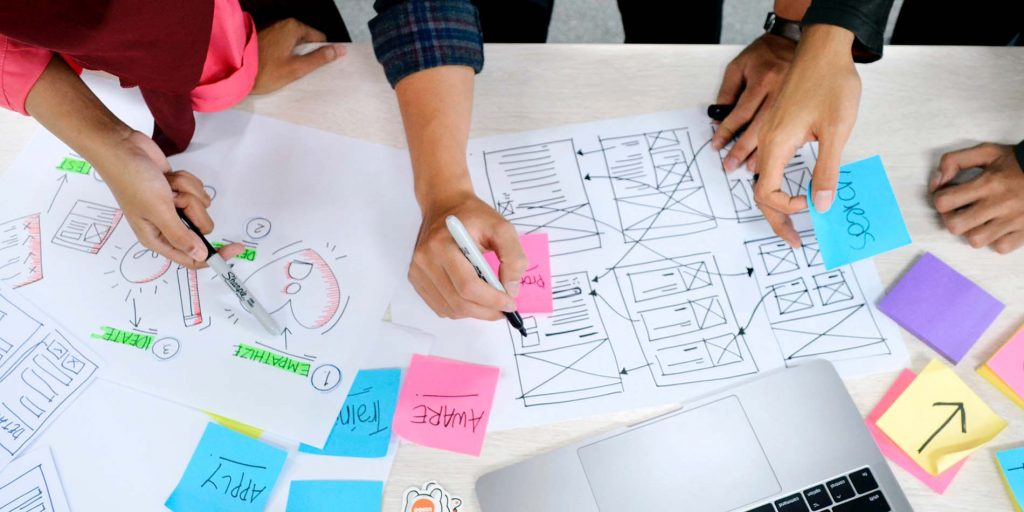 Top down view of a table with hands creating illustrations, wireframes, and making notes on stickies