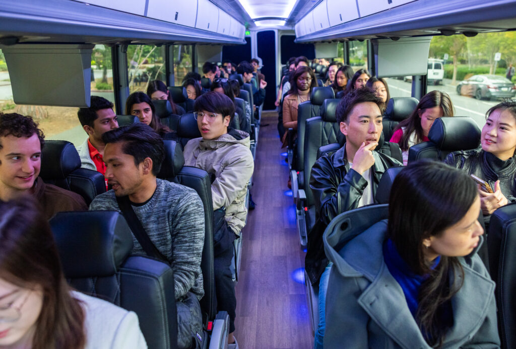 Graduate students fill a futuristic bus, chatting with each other.