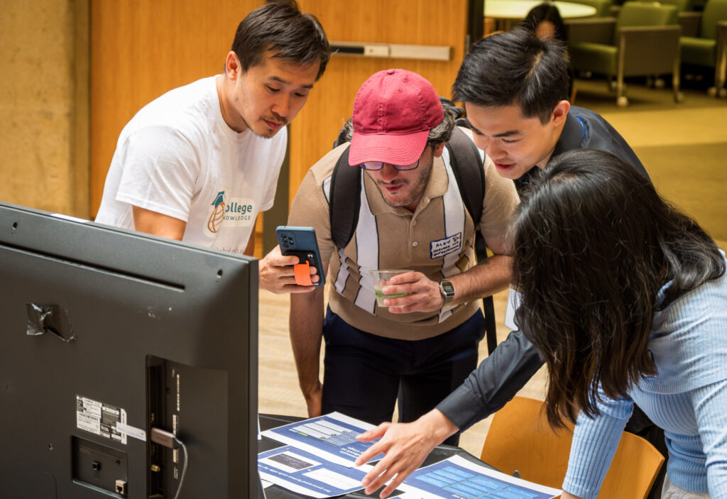 Four students look at a presentation on a table in front of a computer.