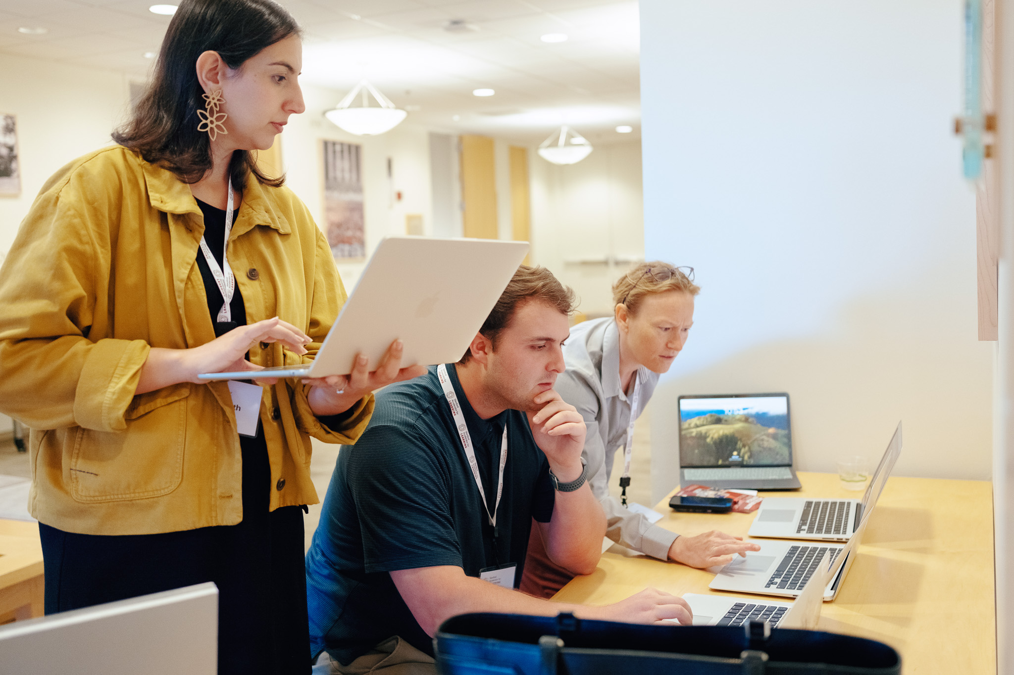 Three adults in business casual wear look at laptops, co-working in a Stanford space.