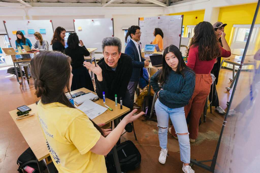 A group of undergraduate and continuing studies students discuss design in an open classroom space.