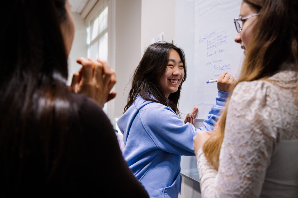A group of students write on a whiteboard.