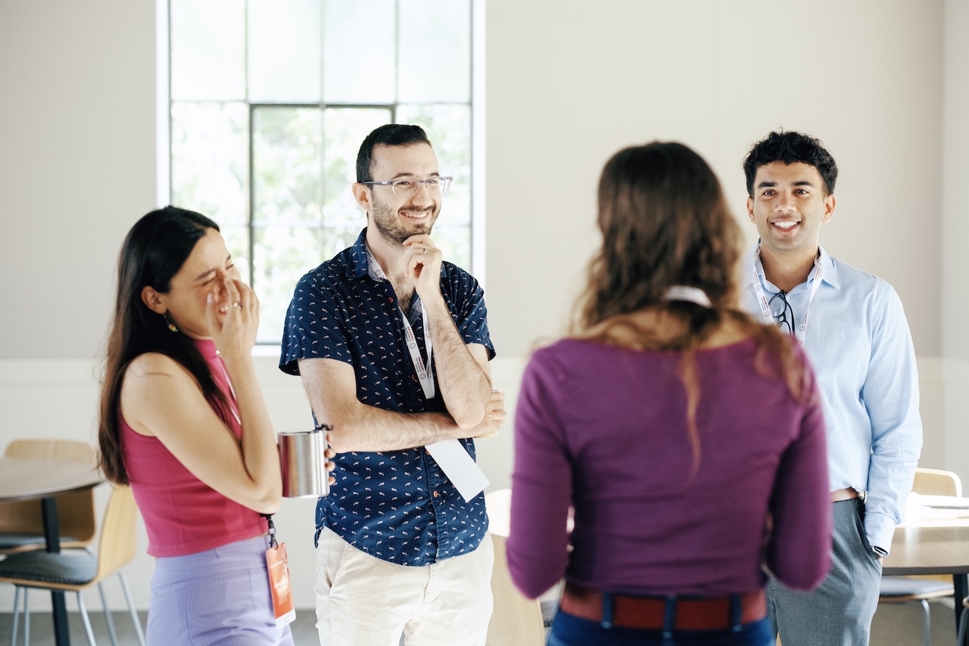A group of students stand together in a conference setting talking and laughing.